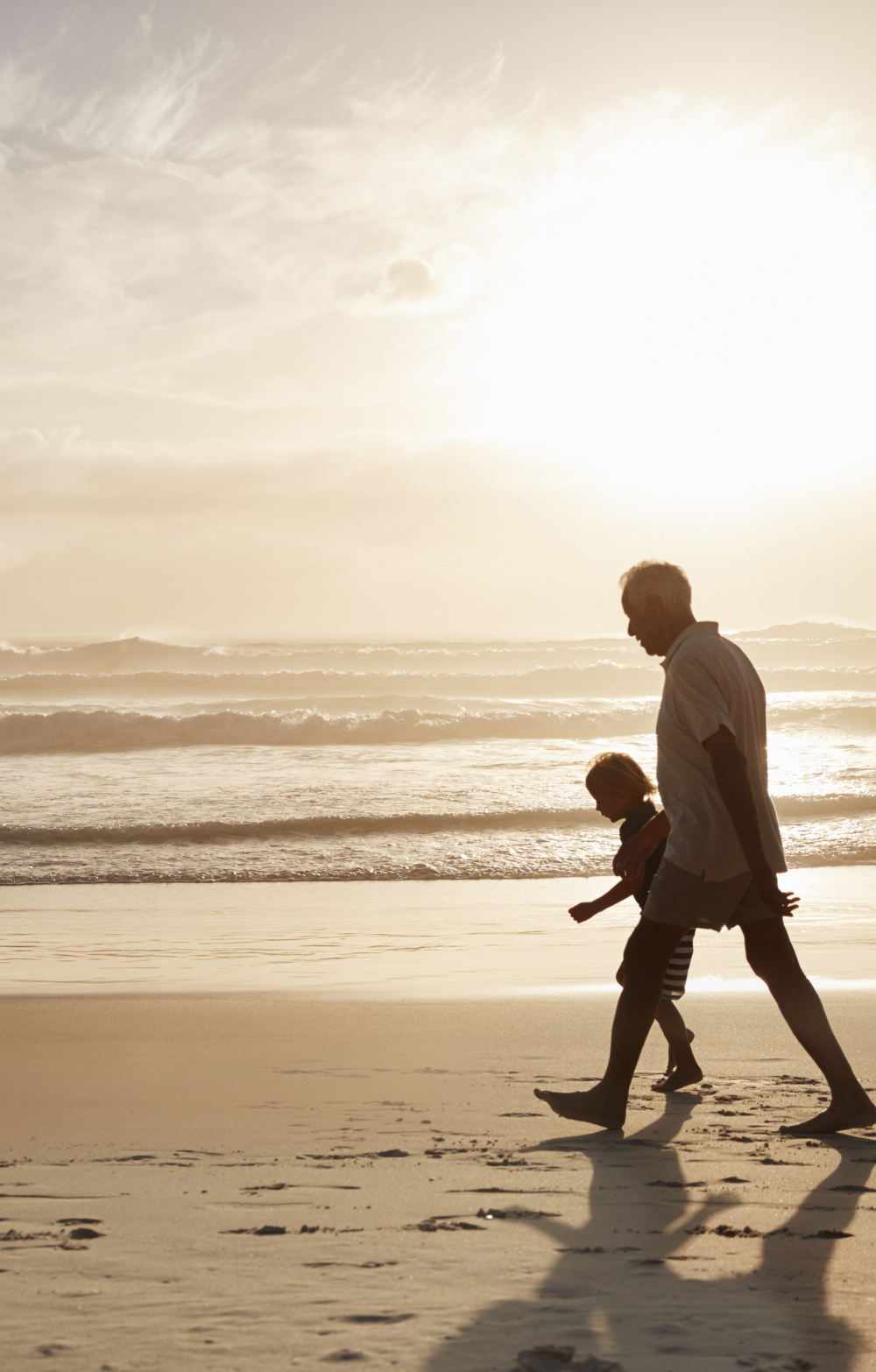 Grandfather with grandchild walking on a beach at sunset