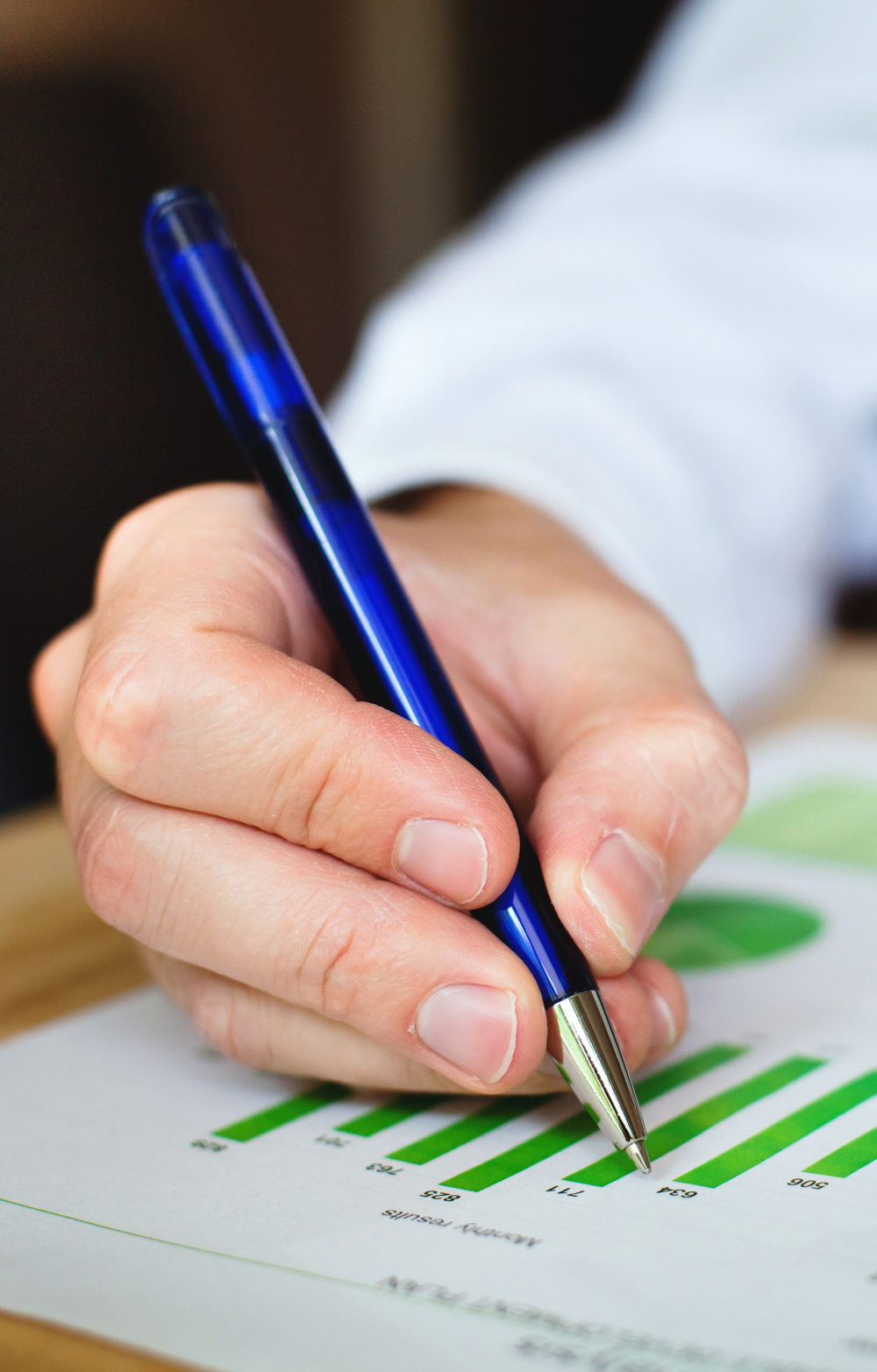 Picture of a pair of hands of a man in a suit marking up a document showing green bar charts