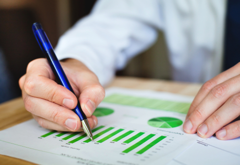 Picture of a pair of hands of a man in a suit marking up a document showing green bar charts